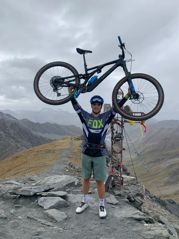 Andrea Murisasco solleva la mountain bike sopra la testa in cima a un colle
